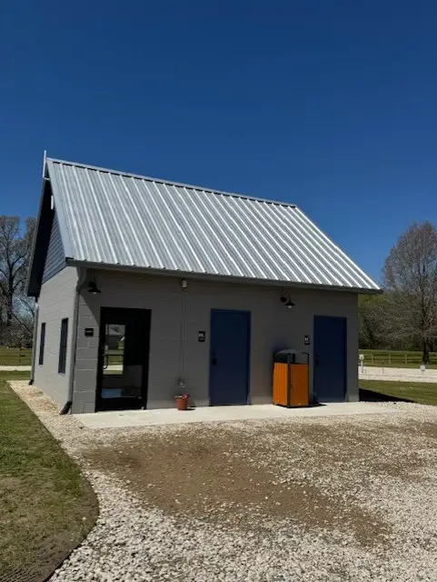 Modern gray block bathhouse building with metal roof, blue restroom doors, glass entry door, and orange trash