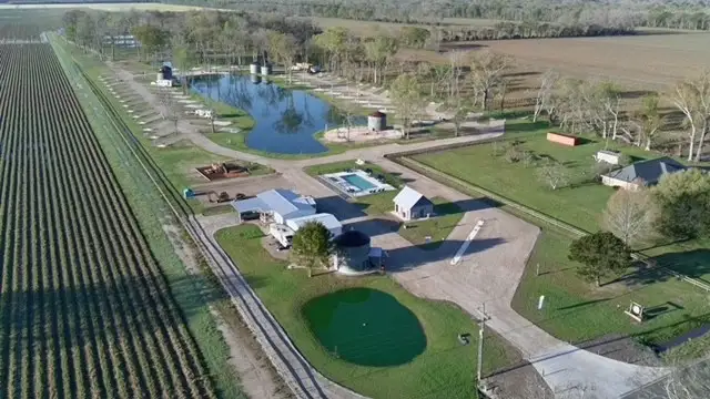 Aerial photo of a rural property with two ponds, a swimming pool, metal barns, silos, and adjacent crop fields.