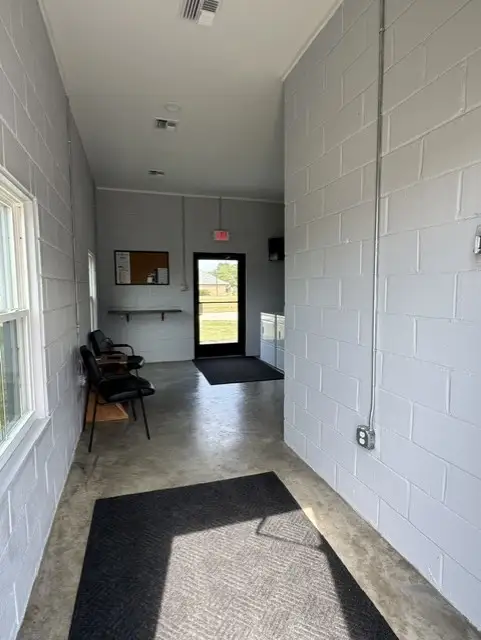 Interior hallway of a white cinder block laundry or office building with chairs, floor mats, bulletin board, and glass